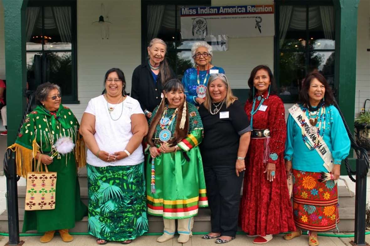 Miss Indian America winners reunited at the Sheridan WYO Rodeo in 2013 and 2015. Shown here in 2015, front row, left to right: Arlene Wesley (Yakama), MIA 1953; Annita Jo Wolf Black representing her mother, Brenda Bearchum (Northern Cheyenne-Yakama), MIA 1961; Williamette Youpee (Sisseton-Yankton Sioux), MIA 1963; Sharon Ahtone Harjo (Kiowa), MIA 1965; Sarah Johnson Luther (Navajo), MIA 1967; Deana Harragarra Waters (Otoe-Kiowa), MIA 1975. Back row, left to right: 1954 Miss Indian America runner-up Annie Grace Strange Owl (Northern Cheyenne); Jewel Medicine Horse Williams (Crow), secretary to Howard Sinclair. Gregory Nickerson photo. Miss Indian America winners reunited at the Sheridan WYO Rodeo in 2013 and 2015. Shown here in 2015, front row, left to right: Arlene Wesley (Yakama), MIA 1953; Annita Jo Wolf Black representing her mother, Brenda Bearchum (Northern Cheyenne-Yakama), MIA 1961; Williamette Youpee (Sisseton-Yankton Sioux), MIA 1963; Sharon Ahtone Harjo (Kiowa), MIA 1965; Sarah Johnson Luther (Navajo), MIA 1967; Deana Harragarra Waters (Otoe-Kiowa), MIA 1975. Back row, left to right: 1954 Miss Indian America runner-up Annie Grace Strange Owl (Northern Cheyenne); Jewel Medicine Horse Williams (Crow), secretary to Howard Sinclair. Gregory Nickerson photo.
