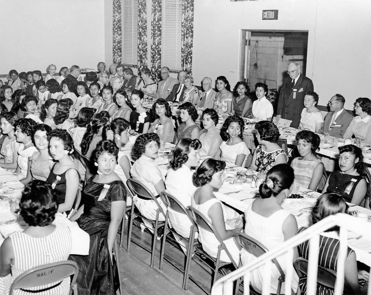 These women wear 1950s party dresses and modern hairstyles at a dinner for Miss Indian America contestants and judges at Sheridan’s Kalif Shrine Mosque. Howard Sinclair is standing. The reigning Miss Indian America would be expected to wear tribal regalia throughout the coming year while serving in her official capacity as a goodwill ambassador. Lochrie Collection, Montana Historical Society. These women wear 1950s party dresses and modern hairstyles at a dinner for Miss Indian America contestants and judges at Sheridan’s Kalif Shrine Mosque. Howard Sinclair is standing. The reigning Miss Indian America would be expected to wear tribal regalia throughout the coming year while serving in her official capacity as a goodwill ambassador. Lochrie Collection, Montana Historical Society.