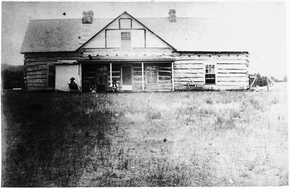 Frewen’s Castle, where young Marth James, a lady’s maid, spent the winter of 1882-1883 with her British employers, the Right Honorable William Cairus Armstrong and his bride, the daughter of General Lushington. Martha married cowboy Frank Bull the following year. The house was by far the most splendid for hundreds of miles in all directions. Large log house with a few people sitting on the front porch and in a chair in the front yard.