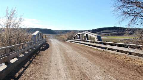 In 1936, the Black and Yellow Trail was reconstructed in the vicinity of Ten Sleep. Portions of the road were realigned, and this single-span Warren pony truss bridge was built to cross the Nowood River just west of Ten Sleep. This route (now Washakie County Road 580A) was abandoned in the 1960s when a new road was built a few hundred feet to the north. One can still drive this county road west toward Worland for several miles to a point where drainages and topography make the road impassable. Authors photo, 2013. In 1936, the Black and Yellow Trail was reconstructed in the vicinity of Ten Sleep. Portions of the road were realigned, and this single-span Warren pony truss bridge was built to cross the Nowood River just west of Ten Sleep. This route (now Washakie County Road 580A) was abandoned in the 1960s when a new road was built a few hundred feet to the north. One can still drive this county road west toward Worland for several miles to a point where drainages and topography make the road impassable. Authors photo, 2013.